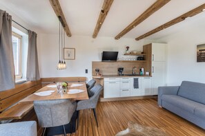 A modern kitchen with wooden beams, a dining area with a wooden table and chairs, and a grey sofa.