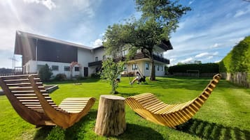 Ein modernes Haus mit großem Rasen, zwei hölzernen Schaukeln und einem Baum.