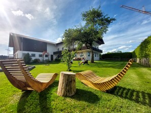 Une maison moderne avec une grande pelouse, deux balançoires en bois et un arbre.