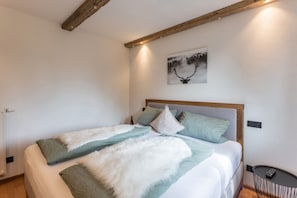 A bed with a wooden headboard, a painting of a deer, and a small table with a remote control.