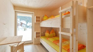 Ein Schlafraum mit Etagenbetten, einem Holztisch und einem Fenster mit Blick auf Gebäude und Bäume.