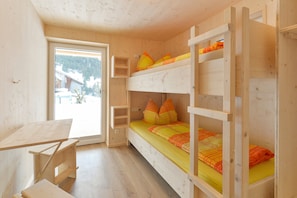 Dormitorio con literas, un escritorio de madera y ventana con vistas a edificios y árboles.
