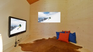 Ein Zimmer mit einem an der Wand befestigten Fernseher, einem großen Fellteppich und einem Bett mit roten und blauen Kissen.