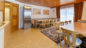 Eine Küche mit Holzausstattung, einem Kühlschrank, einem Esstisch mit Stühlen und einem Teppich.