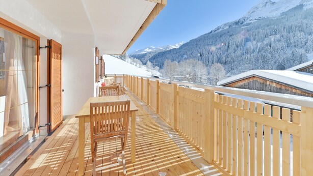Eine Holzterrasse mit Tisch und Stühlen mit Blick auf eine verschneite Berglandschaft.
