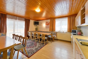 Une pièce aux murs lambrissés, comprenant une table à manger, des chaises, un coin cuisine et un téléviseur.