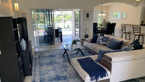 Ein modernes Wohnzimmer mit einer Couch, einem Couchtisch und einem durch Glastüren einsehbaren Essbereich.