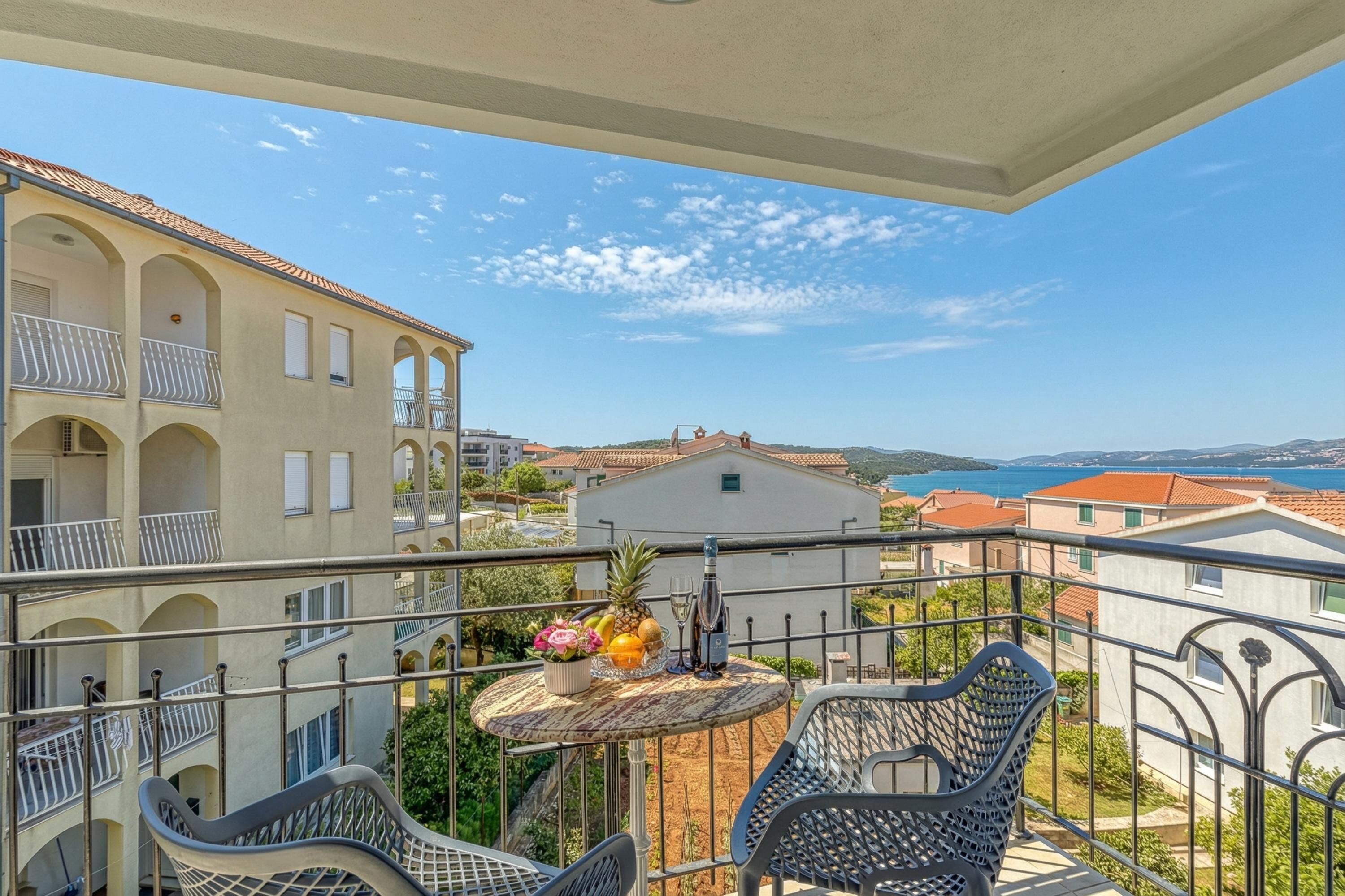 Un balcón con una mesa para dos, una silla y vistas a edificios y al mar.