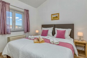 Un lit bien fait, avec des oreillers, une lampe de chevet, une fenêtre avec des rideaux et un tableau accroché au mur.