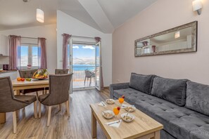 Un salon moderne avec un canapé gris, une table à manger avec des chaises, un coin repas pour le petit-déjeuner et un balcon avec vue.