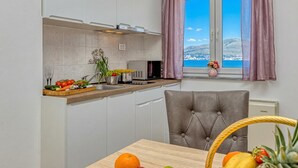 Eine Küche mit Meerblick, einem Esstisch mit Früchten und einem grauen Polsterstuhl.