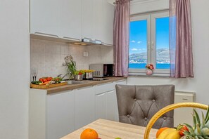 Eine Küche mit Meerblick, einem Esstisch mit Früchten und einem grauen Polsterstuhl.