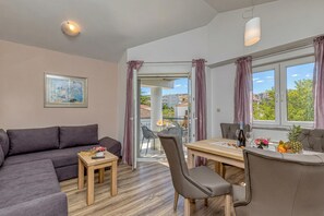 A modern living room with a sofa, a dining table with chairs, a small table with a remote control, and a window with curtains. - Apartment Rafaela 220m from the beach, Okrug Gornji, Croatia (Okrug Gornji)