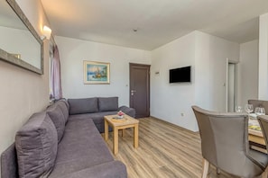 A living area with a sofa, a small wooden table, a TV mounted on the wall, and a door. - Apartment Karlo 220m from the beach, Okrug Gornji, Croatia (Okrug Gornji)