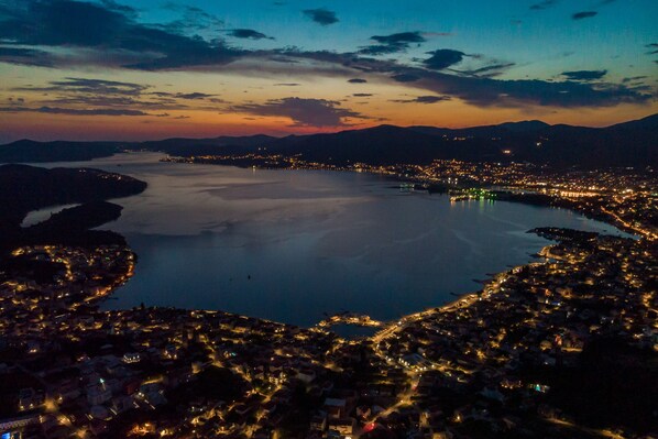 Vista aérea de una ciudad costera al atardecer, con una gran masa de agua en el centro, rodeada de edificios densamente agrupados e iluminada por las luces de la ciudad.