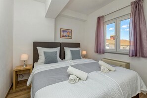 Une chambre avec deux lits, une fenêtre avec des rideaux, une table de chevet avec une lampe et un tableau au mur.