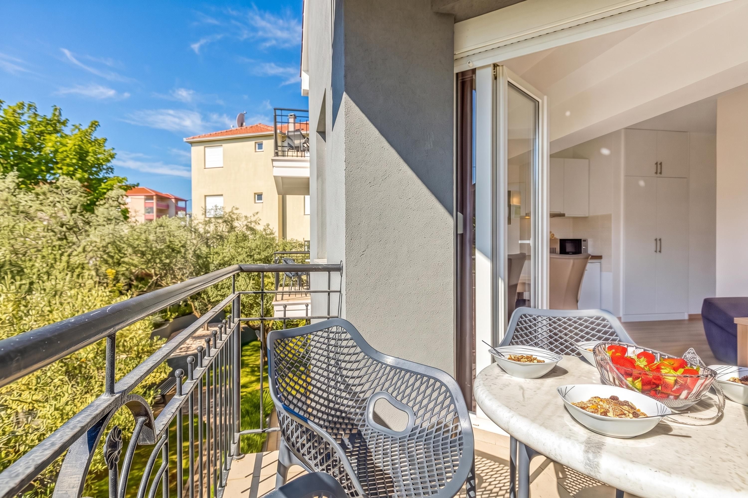 A balcony with a table and chairs, a view of a building, and a door leading to an interior space.