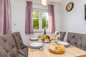 Ein Essbereich mit einem Tisch für zwei Personen, einer Wanduhr und einem Fenster mit Vorhängen.