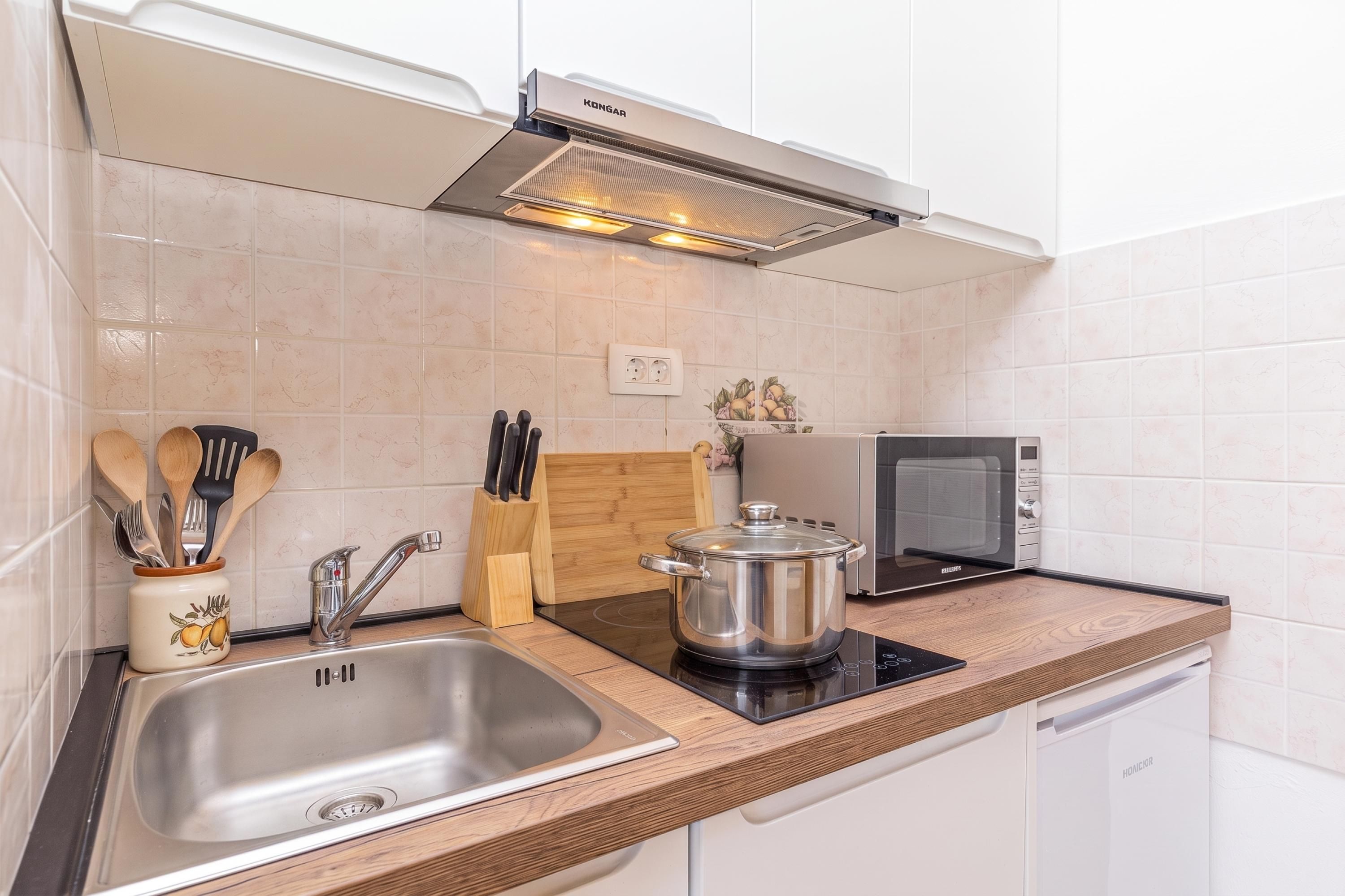 Une cuisine moderne avec un évier en acier inoxydable, un four à micro-ondes, une casserole sur une plaque de cuisson à induction et des ustensiles de cuisine en bois rangés dans un porte-ustensiles.