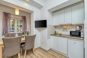 Una cocina compacta con armarios blancos, microondas, hervidor y televisor de pantalla plana.