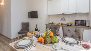 A modern kitchen with white cabinets, a flat-screen TV, and a dining area set with plates, cutlery, and a fruit platter. - Apartment Angie 220m from the beach, Okrug Gornji, Croatia (Okrug Gornji)
