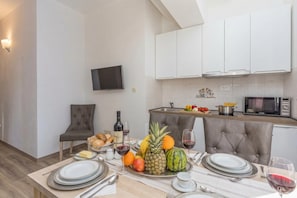 Une cuisine moderne avec des meubles blancs, un téléviseur à écran plat et un coin repas agrémenté d’assiettes, de couverts et d’un plateau de fruits.