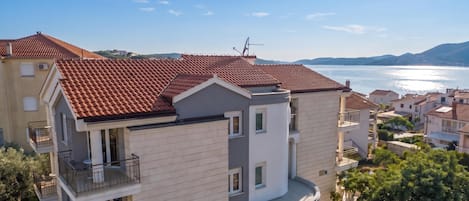 A multi-story residential building with a red-tiled roof, balconies, and a view of a body of water.