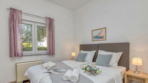 A neatly made bed with pillows, a bedside table with a lamp, and a window with curtains. - Apartment Angie 220m from the beach, Okrug Gornji, Croatia (Okrug Gornji)
