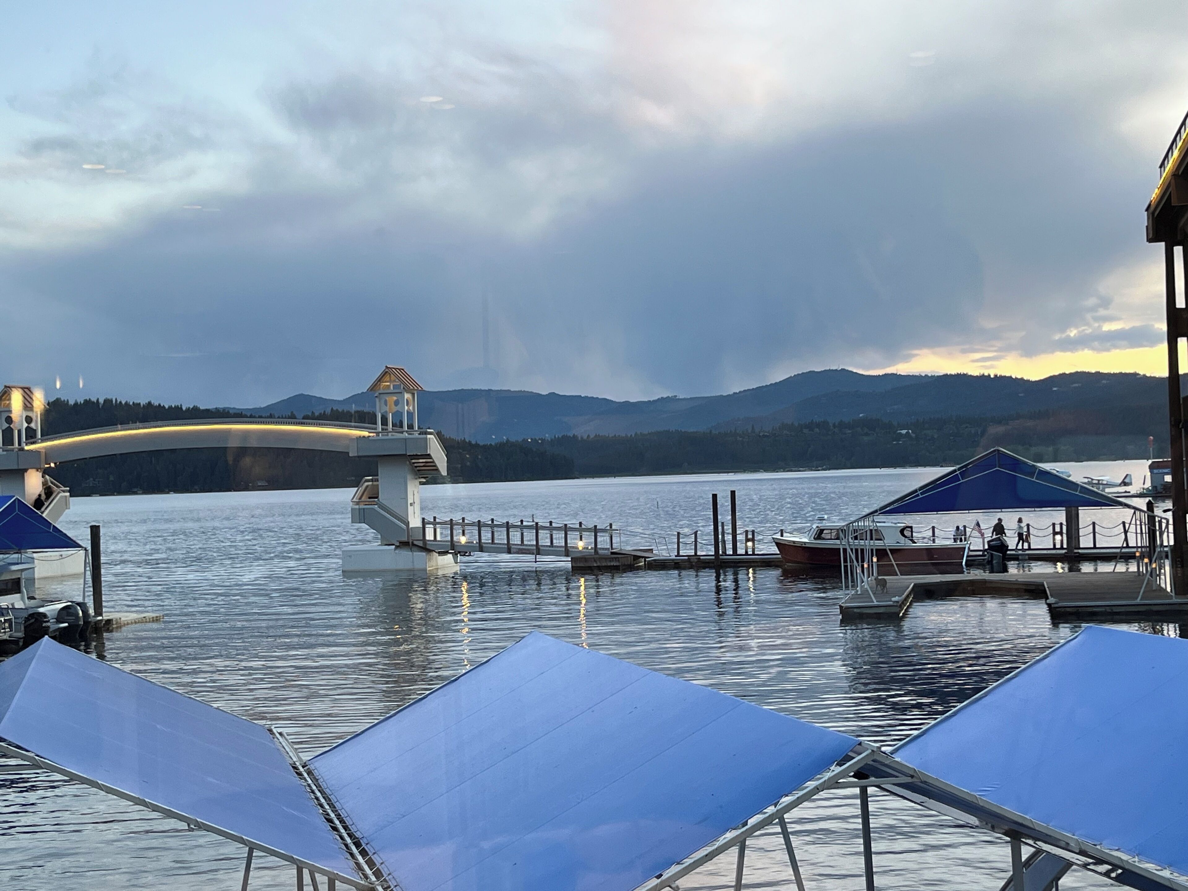 A waterfront area with a bridge, boats, and a dock with a covered seating area.