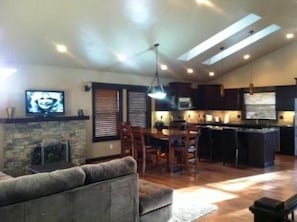 Uma sala de estar com lareira, um espaço de jantar com mesa e cadeiras, e uma cozinha com armários escuros e um micro-ondas.