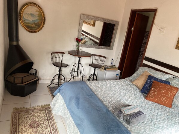 A bedroom with a bed, a small table with two chairs, a mirror, a heater, and a door. - Charming place, suite with fireplace. (RJ)