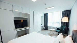 A hotel room with a bed, a desk, a television, a chair, a lamp, and a window with curtains. - Celeb Stay Songdo (Incheon)