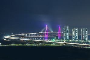 A nighttime view of a modern bridge with illuminated structures, a city skyline in the background, and a well-lit roadway. - Celeb Stay Songdo (Incheon)