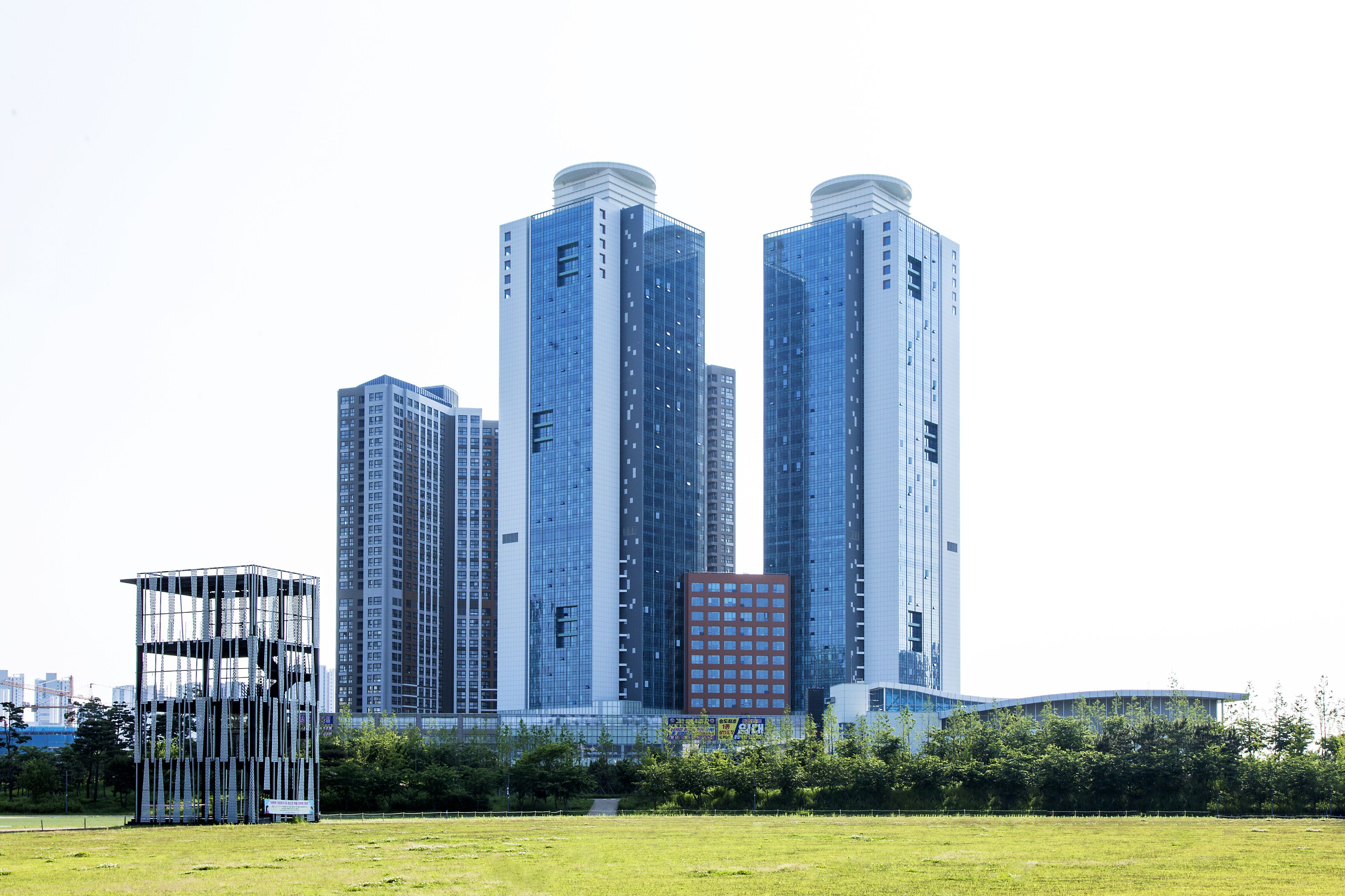Un immeuble moderne de grande hauteur, avec une section centrale de couleur rouge, entouré de verdure et d’autres bâtiments.
