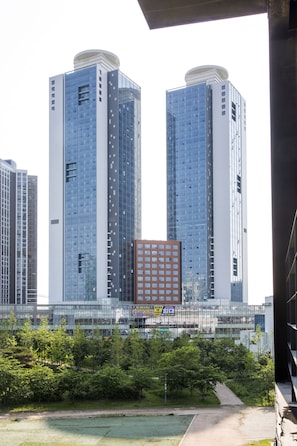 A modern high-rise building with a glass facade, surrounded by greenery and a smaller adjacent building. - Celeb Stay Songdo (Incheon)