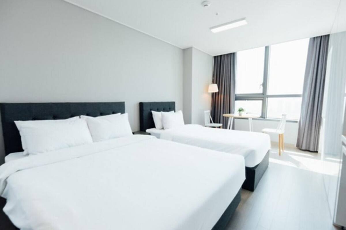 Habitación de hotel con dos camas, una mesita, una silla y un ventanal con cortinas.