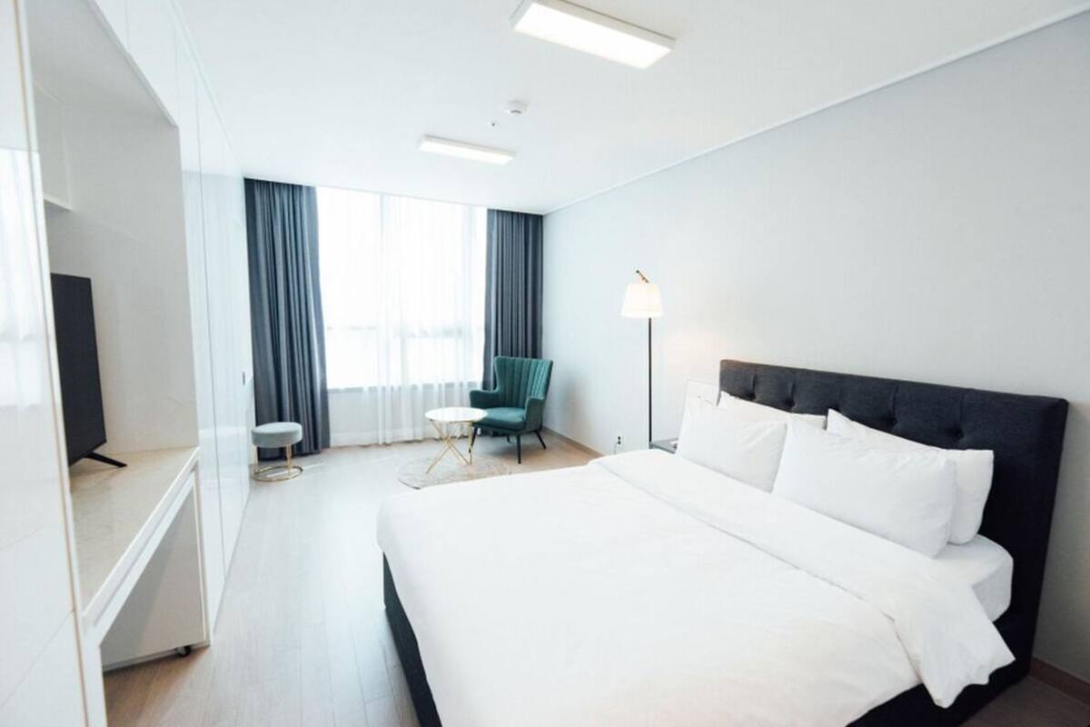 Habitación de hotel con una cama grande, un escritorio, una silla, una lámpara y vistas al exterior.