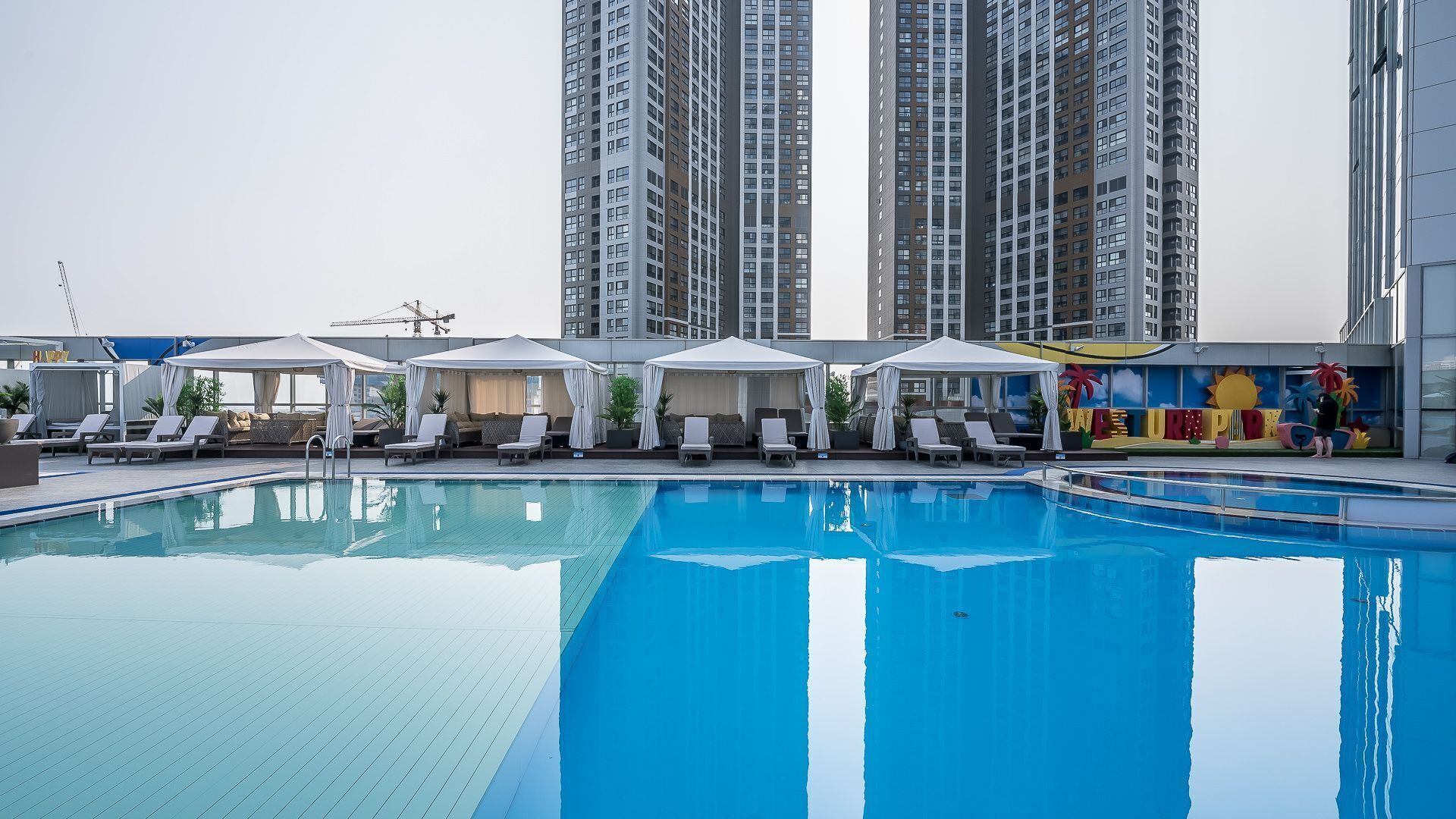 Una piscina con sillas de descanso y sombrillas, rodeada de edificios altos.