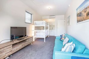 Quarto com televisão, beliches, sofá e cozinha.