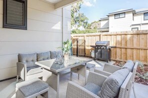 An outdoor patio with wicker furniture, a glass-top table, and a barbecue grill.