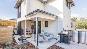 A two-story house with a covered patio area, a barbecue grill, and a dining set.