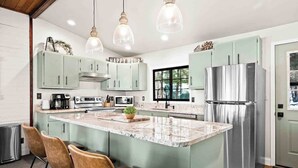 Une cuisine moderne dotée d’un îlot central, d’appareils électroménagers en acier inoxydable et de meubles de couleur vert clair.