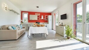 A modern living room with a sofa, dining table, and a kitchen area with a red accent wall. - Residenza Cantalupo – Relax Oasis with Poo l Ap38 (Imperia)