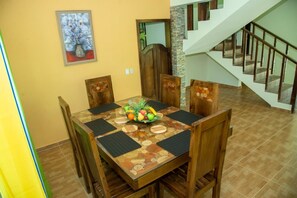 A dining area with a wooden table and chairs, a fruit bowl centerpiece, and a staircase in the background. - Villa del Baiguate #3 (Jarabacoa)