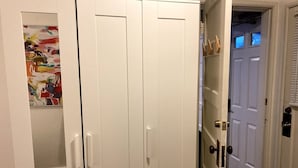 A hallway with a white wardrobe, a door with a window, and a colorful abstract painting on the wall.