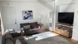 A living room with a sofa, a blue armchair, a TV, and a painting on the wall.
