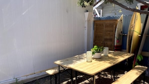 A wooden table with benches, surrounded by a white fence, with surfboards leaning against the fence.