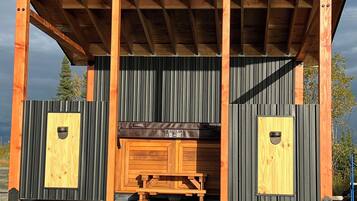 A covered outdoor area with a wooden bench and two doors, surrounded by metal siding and a gravel ground.