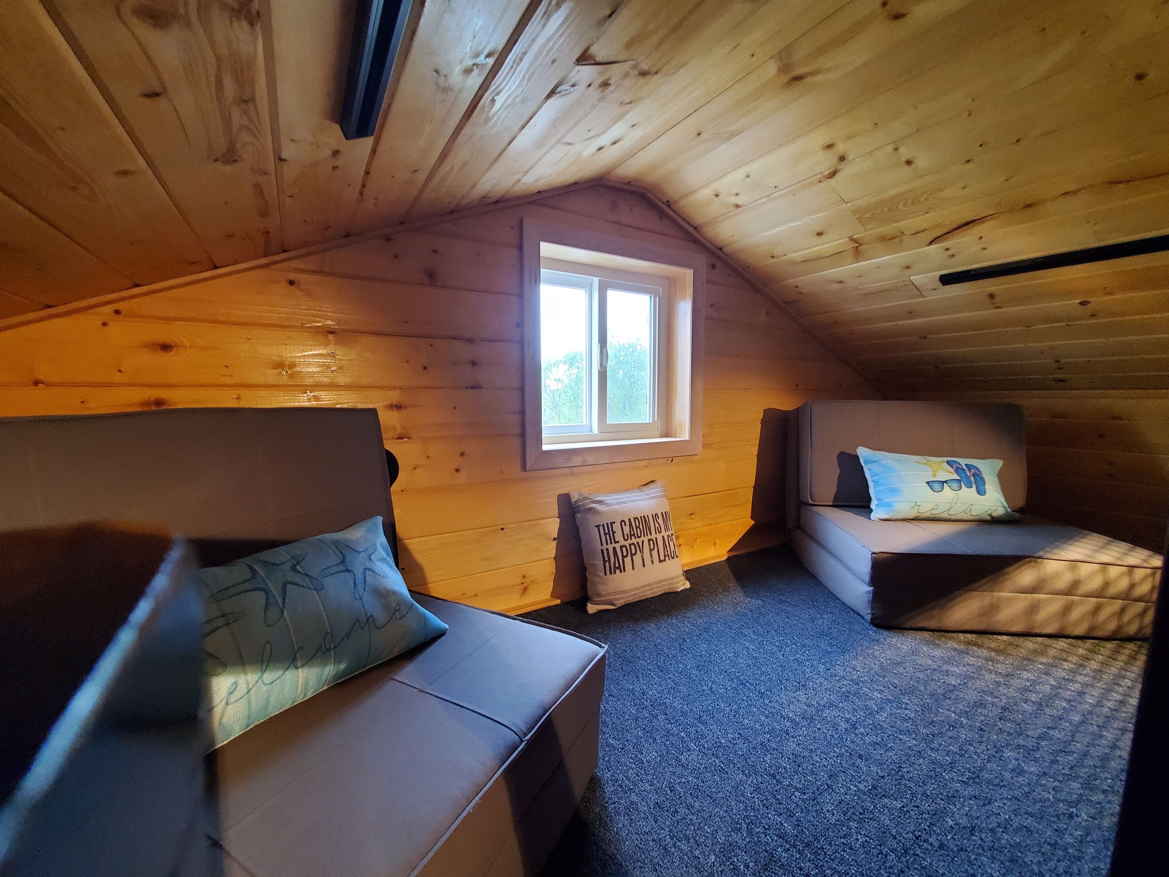 A cozy attic bedroom with two sofas, a window, and a ceiling vent.