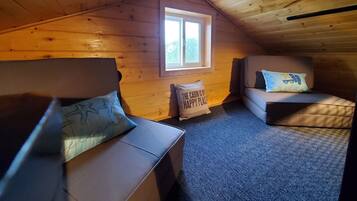 A cozy attic bedroom with two sofas, a window, and a ceiling vent.